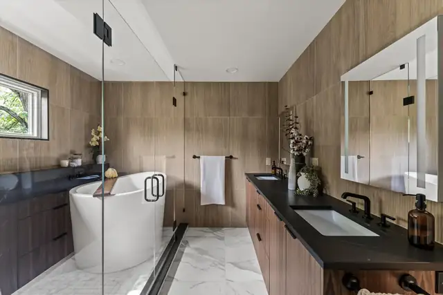 Huron River primary suite bathroom with a freestanding tub, wood-look wall tile, black countertop and floating wood vanity
