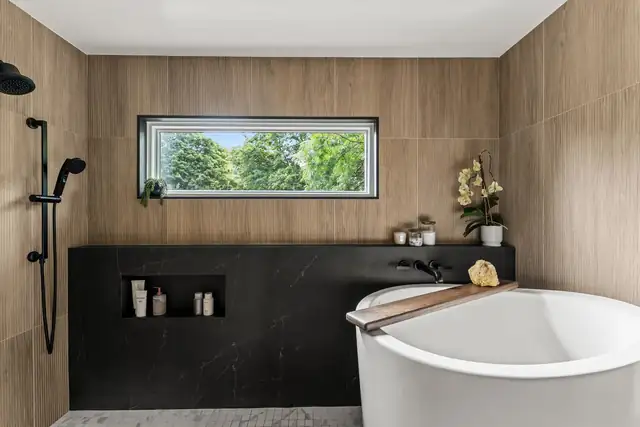 Huron River primary bathroom with a freestanding tub, wood-look wall tile, a black stone ledge and a wide window