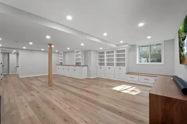 Finished lower level with white built-in cabinets, open shelving, a wood support post and light wood-look flooring