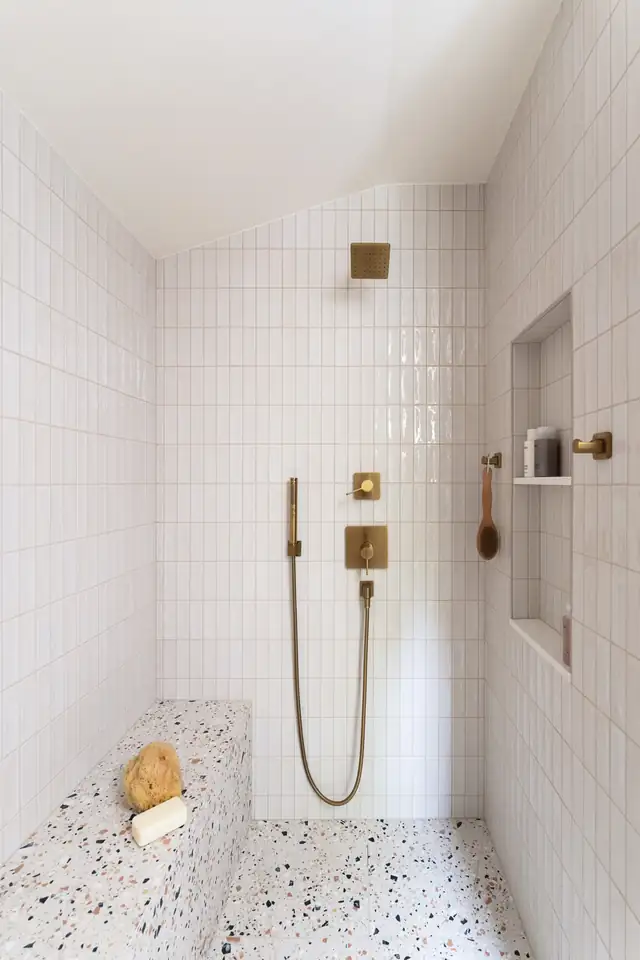Shower in the Emerald Addition with white stacked wall tile, brass fixtures, a niche and a terrazzo bench