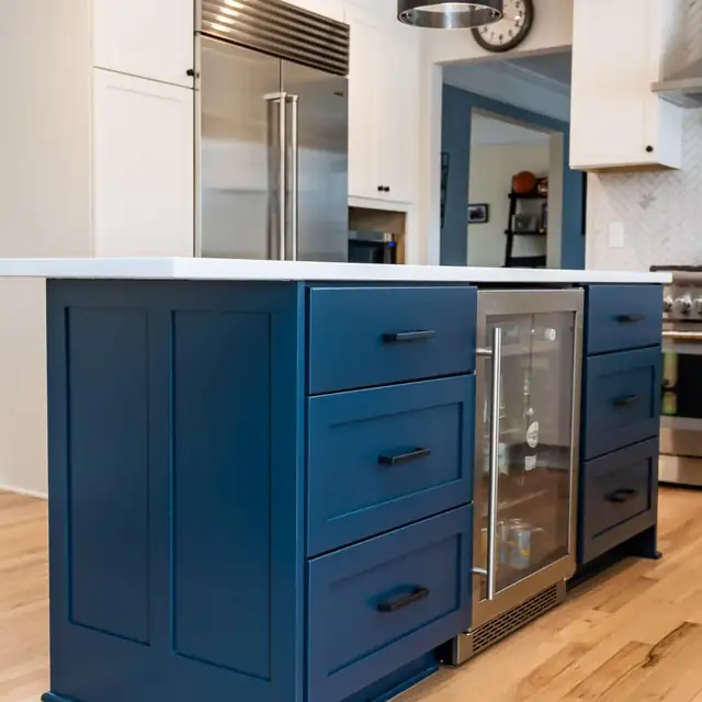 Navy blue kitchen island with drawer stacks, black pulls and a built-in beverage fridge