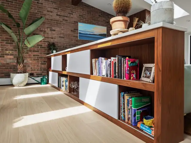 Custom walnut built-in bookcase and cabinet run beside an exposed brick wall