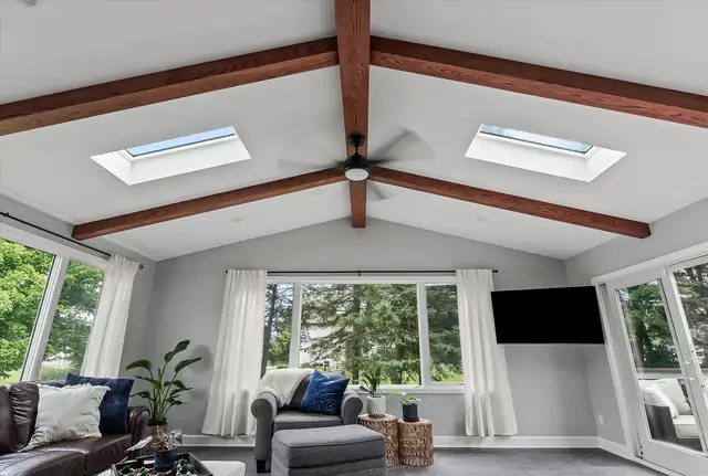 Sunroom addition with exposed wood beams, two skylights, a ceiling fan and windows on three sides