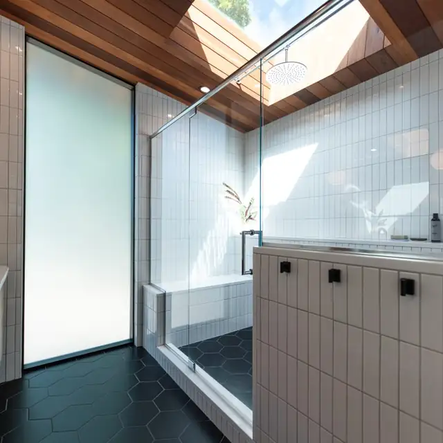 Walk-in shower under a skylight with a glass panel, white wall tile and black hexagon floor tile