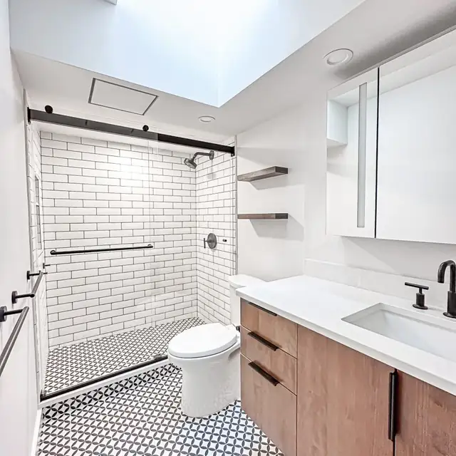 Bathroom with a white subway tile shower, black and white patterned floor tile, a skylight and a wood vanity